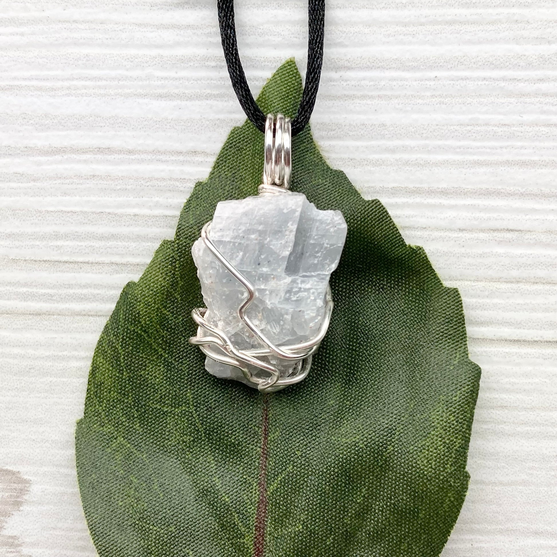 Natural Blue Calcite Necklace. Blue Calcite crystal wrapped with tarnish resistant silver colored copper wire. Pendant comes on a black lobster claw necklace with silver ends.