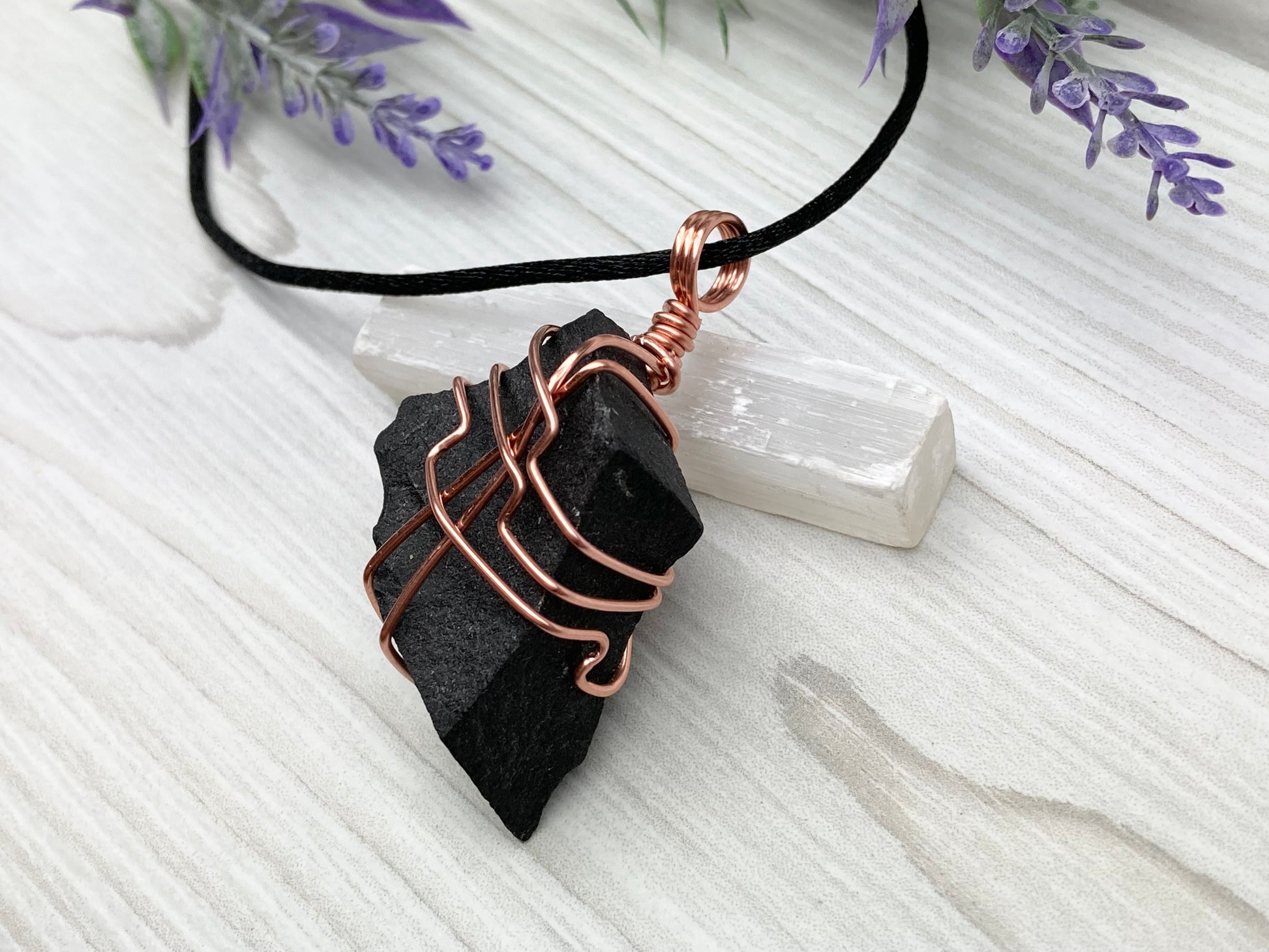 Black Agate stone wrapped with copper wire. Comes on a black satin silk necklace.