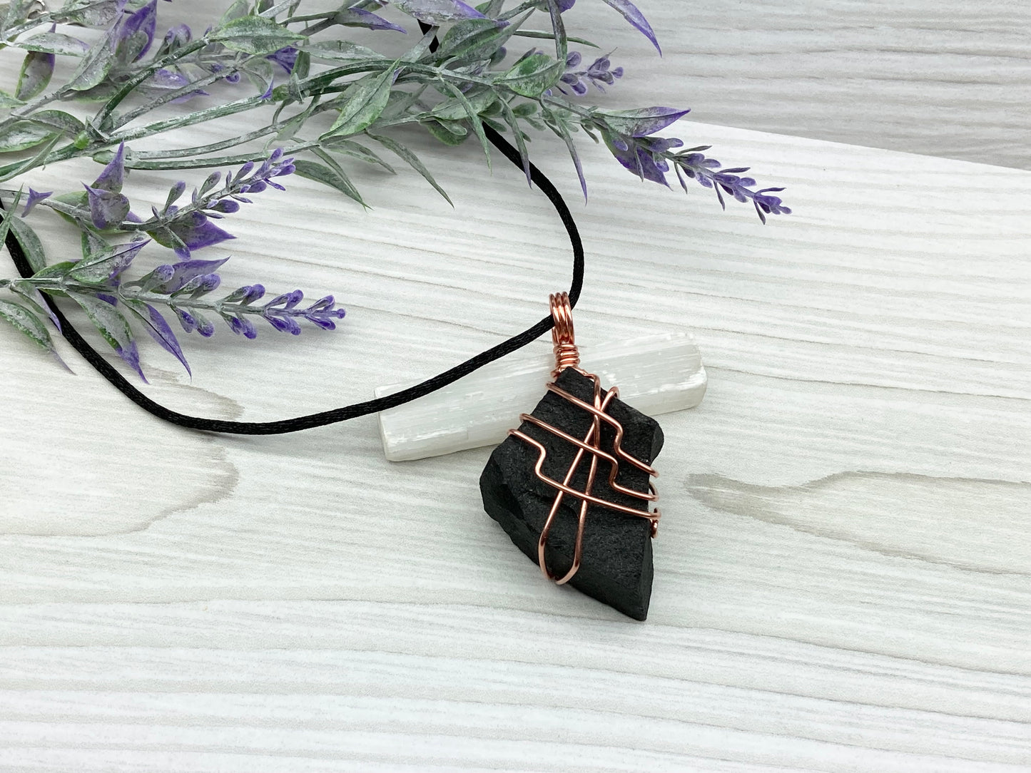 Black Agate stone wrapped with copper wire. Comes on a black satin silk necklace.