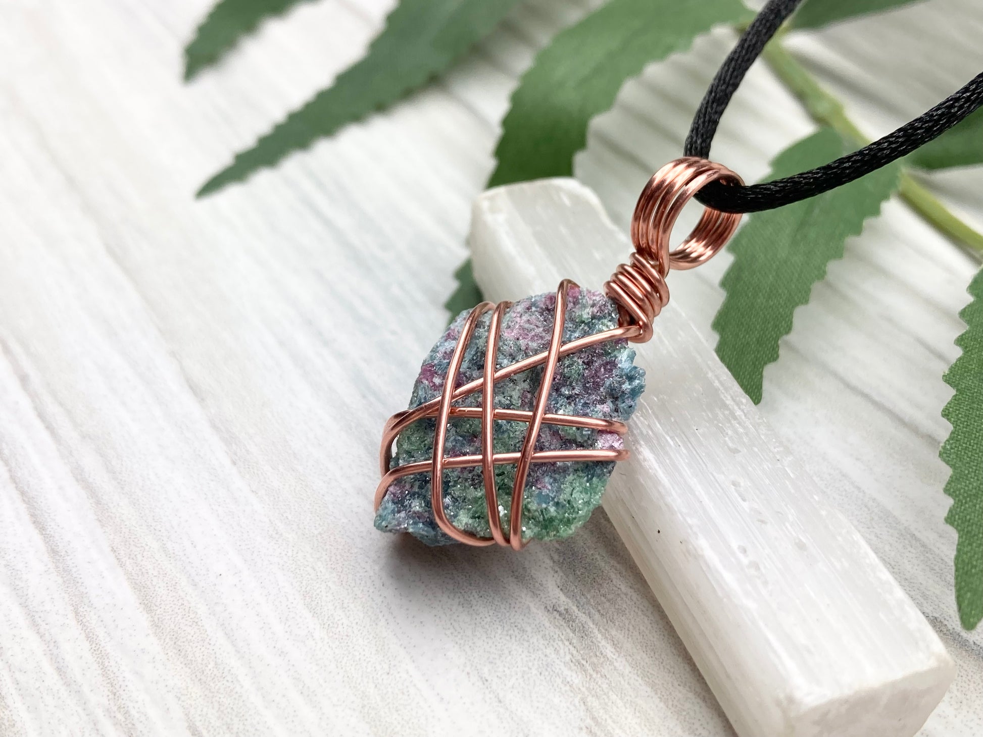 Raw Ruby Zoisite Necklace. This Ruby Zoisite Crystal Is Hand Wrapped With Pure Copper Wire For A Pendant. This Stone is Blue, Red And Green Colored. Comes On A Black Chain. Spiritual New Age Style Jewelry. Left Side View.