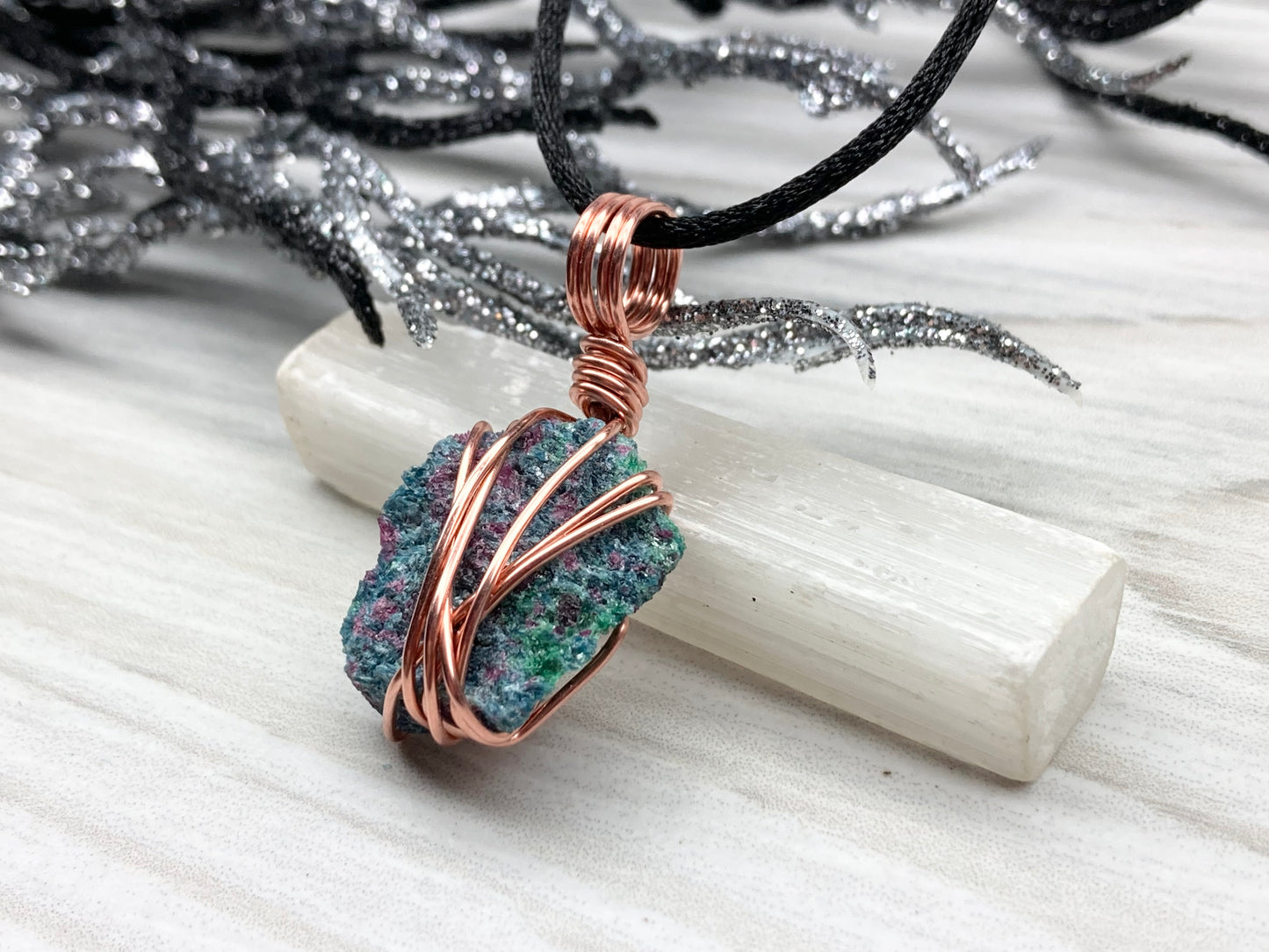 Real Raw Ruby Zoisite Necklace. Left Side View. This Ruby Zoisite Crystal Is Hand Wrapped With Pure Copper Wire. This Stone is Blue, Green and Red Colored. Gemstone Comes On A Black Chain. Boho Spiritual Style Unisex Jewelry.